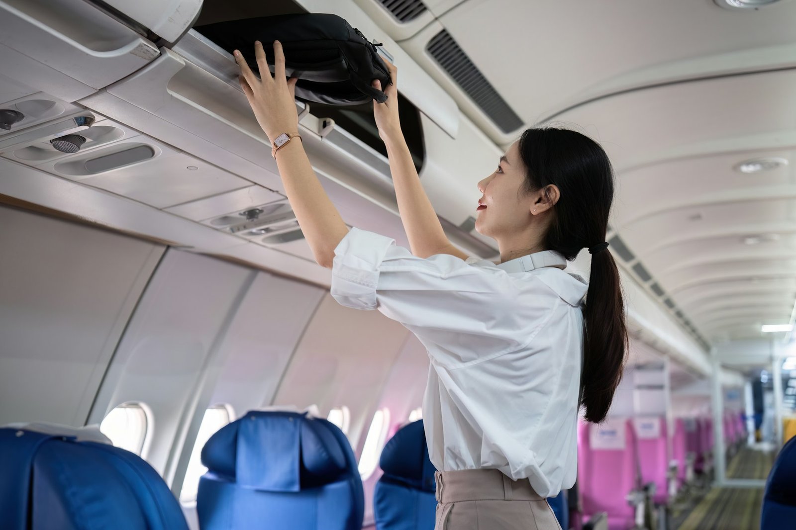 Young woman traveling by plane put her bag in the luggage compartment of the plane.